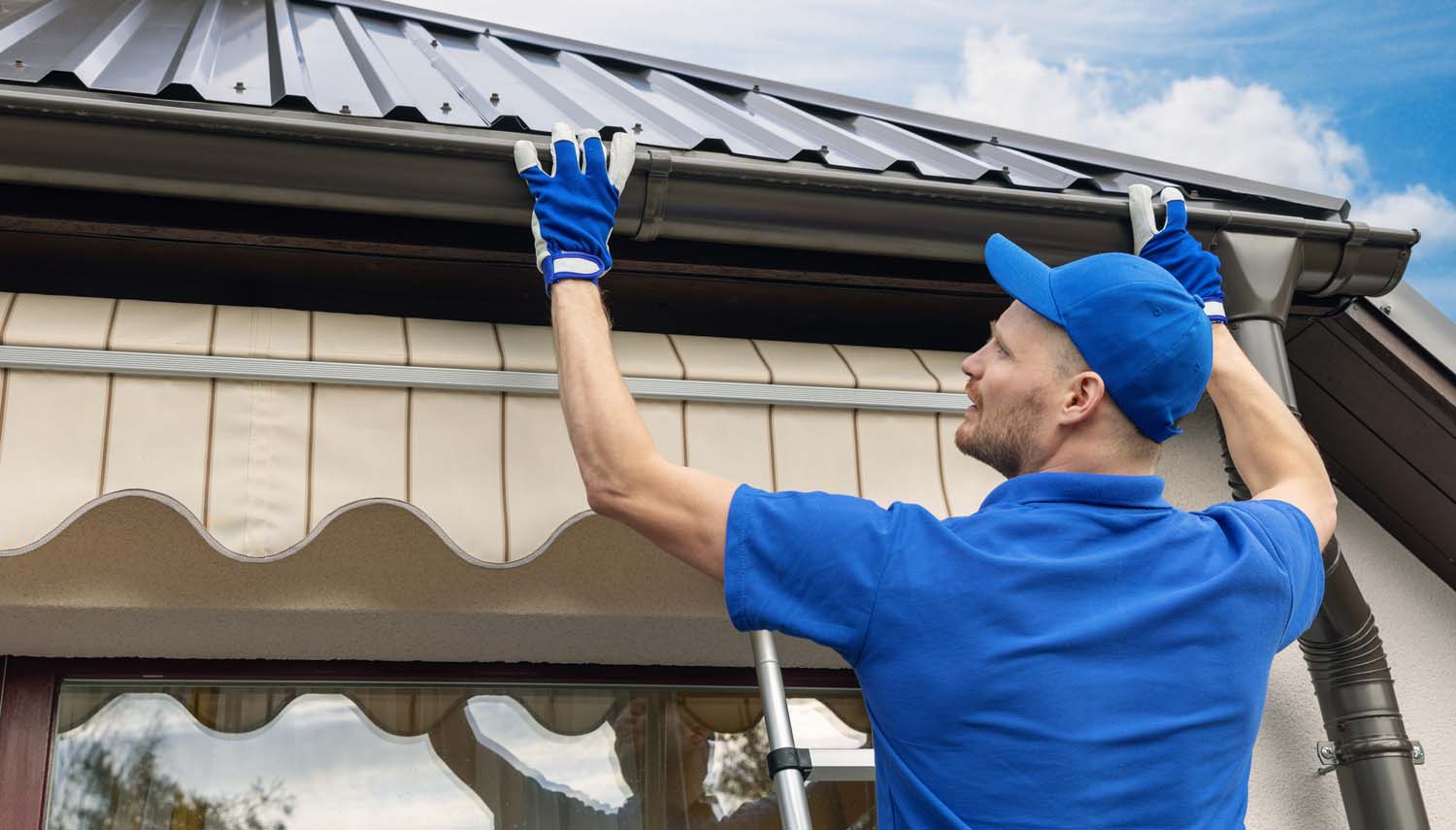 a contractor with a cap is on a ladder inspecting for gutter repair san antonio