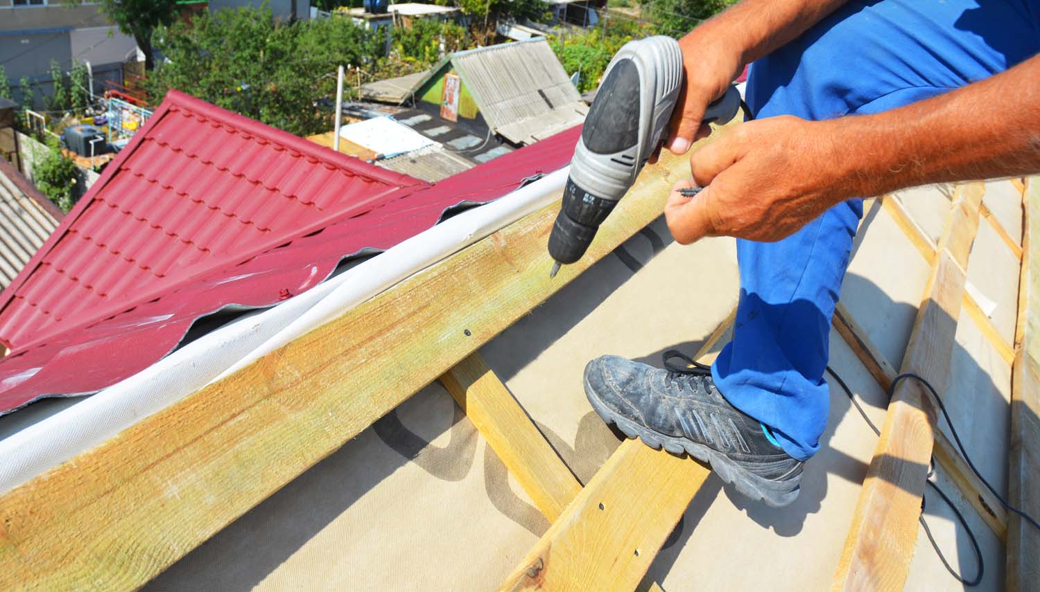 a roofing contractor fastening new metal tiles on a roof in with a drill in San Antonio. TX