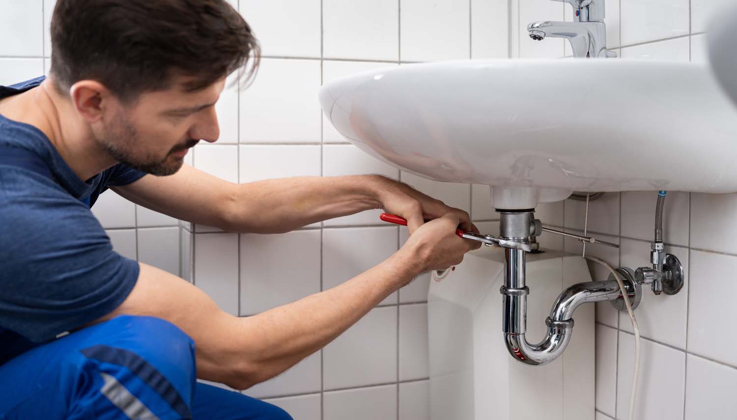 contractor repairing a leaky sink in the bathroom under the sink