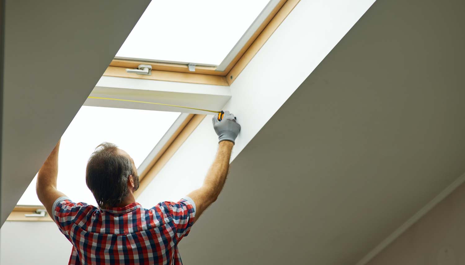 contractor is reaching over his head to install a window in a san antonio attic room