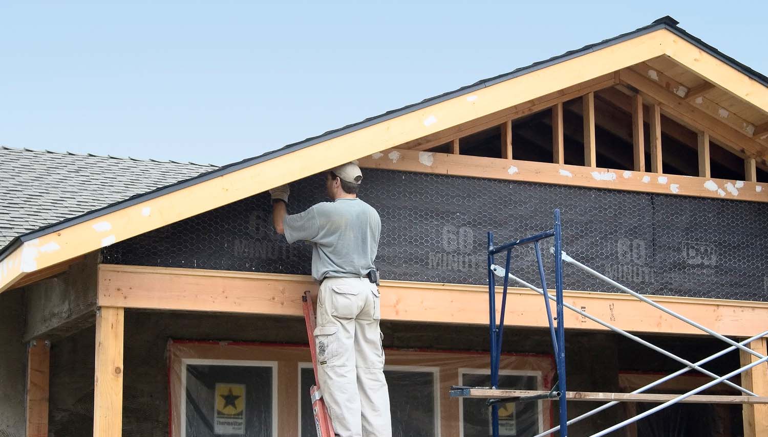 A craftsman installing siding at the exterior of the house.