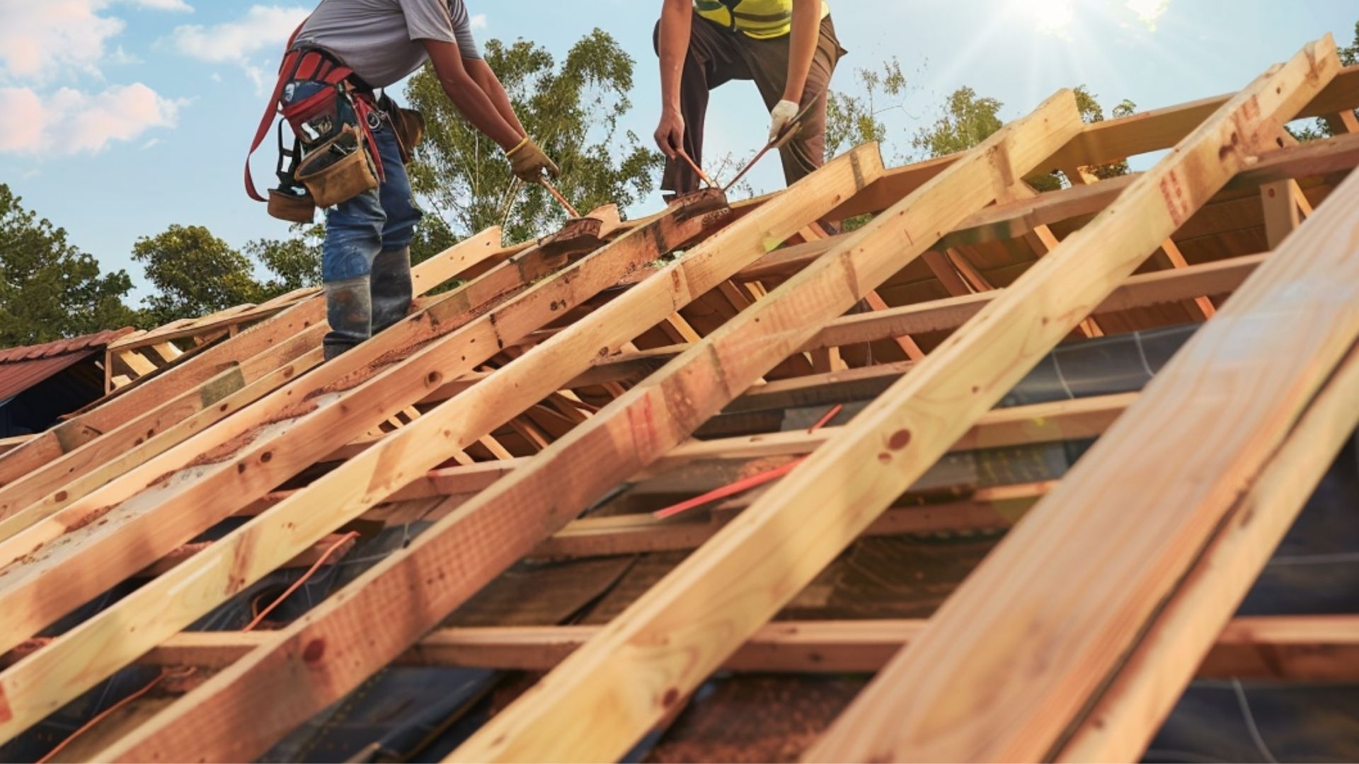 Two roofers are installing a roof wood truss on a suburban house.