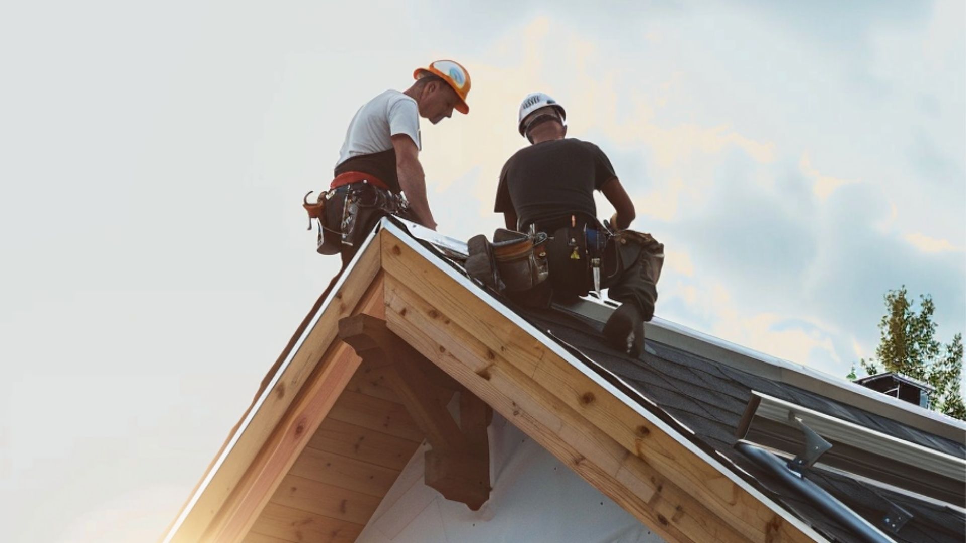 Two roofers at the peak of the roof are focused on repairing the house's roof.